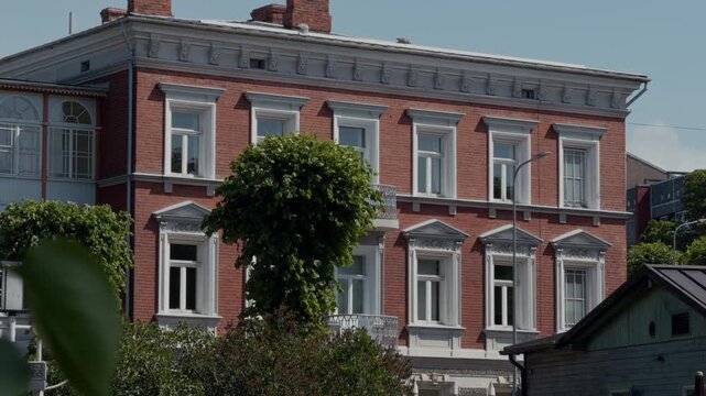 Historic red brick residential building with ornate white trim, tall windows, and leafy foreground