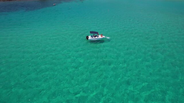 Aerial drone view of a powerful speed boat gliding across crystal-clear turquoise water, creating a striking white wake. Perfect representation of luxury travel, freedom, summer adventure.