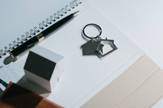 Office desk still life with notebook, pen, house key ring, and small model home on clean workspace