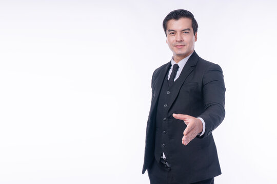 Confident handsome businessman in dark suit extending hand for handshake on white background with copy space. Professional executive welcoming partner or offering business agreement.