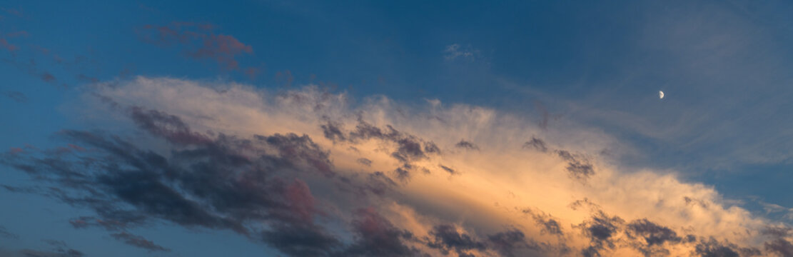 Panoramic view of blue evening sky with dramatic sunset clouds and crescent moon