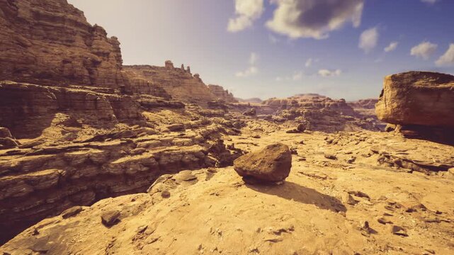 sunlit canyon plateau with expansive vista showcasing layered sandstone cliffs scattered boulders deep ravines clear sky warm golden tones high contrast shadows