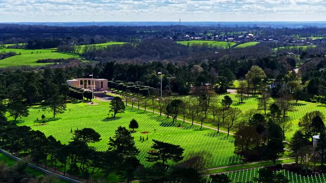 Aerial view of the Normandy American Cemetery and Memorial with rows of white crosses set in green lawns surrounded by trees in Colleville-sur-Mer, France.