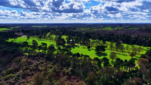 Aerial view of the Normandy American Cemetery and Memorial with rows of white crosses on green lawns surrounded by trees in Colleville-sur-Mer, Normandy, France.