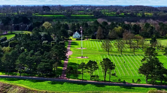 Aerial view of Normandy American Cemetery and Memorial with rows of white crosses on green lawns, surrounded by trees and coastal landscape in Colleville-sur-Mer, France.