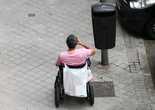 Persona en silla de ruedas diverso funcional con movilidad reducida y bote de bebida y papelera en acera calle discapacitado minusv&aacute;lido