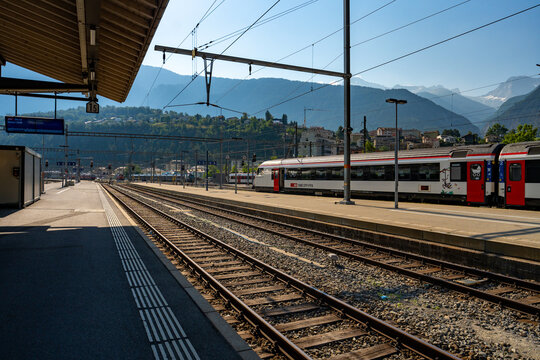 Swiss SBB passenger train at outdoor station platform with mountain scenery in Brig, Valais, Switzerland on sunny day