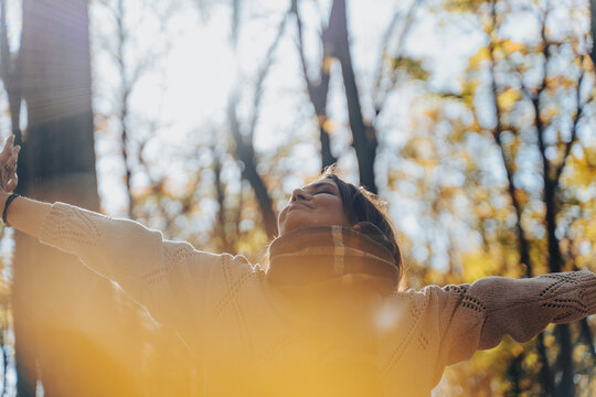 Mature Caucasian woman in warm sweater and scarf enjoying fresh air in autumn forest. Mental health and healthy aging concept