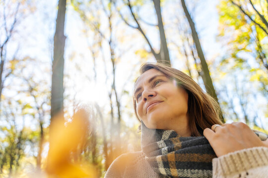 Mature Caucasian woman in warm sweater and scarf enjoying fresh air in autumn forest. Mental health and healthy aging concept