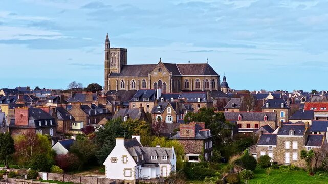 Aerial view of a historic stone church rising above the slate rooftops and lush greenery of a traditional French town, France.