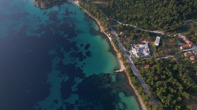 Aerial drone of a peaceful beach in Thassos, Greece, featuring transparent turquoise water, paddleboards, swimmers and a beautiful Mediterranean coastline.