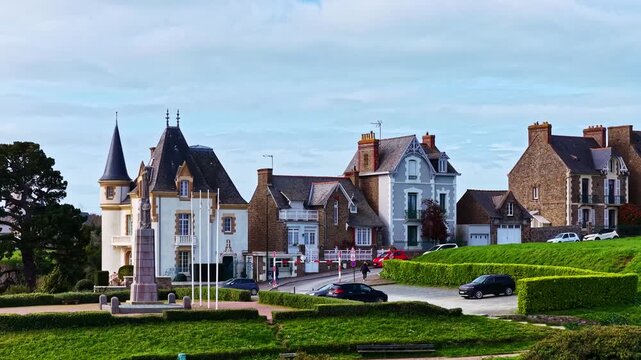 Aerial view of a historic war memorial in a quiet town square surrounded by traditional stone houses and lush green hedges in France.
