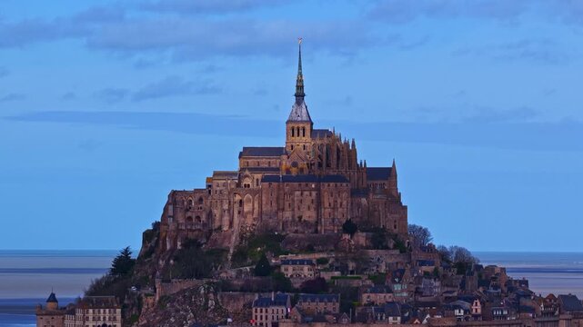 Aerial view of the historic Mont Saint-Michel abbey perched on a rocky island surrounded by tidal flats under a clear blue sky in France.