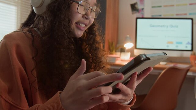 Asian female teenager wearing headphones using digital tablet in room at night. Perfect for online education, e-learning platforms, and educational app marketing campaigns