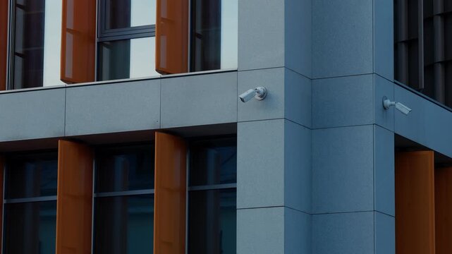 Modern building facade with orange window louvers, gray panels, and security cameras