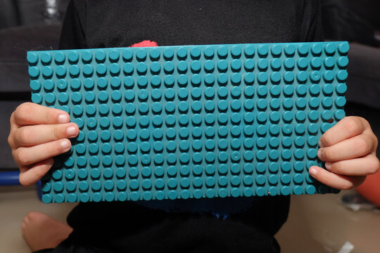 child holding a rectangular green plastic toy building baseplate horizontally in front of their chest.