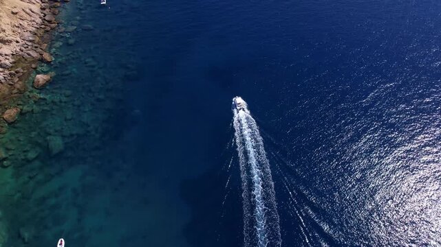 Aerial view of a fast motor yacht cutting through crystal-clear blue water. Vibrant textures, dynamic waves, powerful motion create the perfect visual for themes of luxury, freedom, vacation.