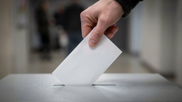 Voter hand places a folded ballot paper into the slot of a plastic box here.