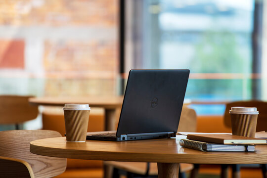 A casual caf&eacute; workspace featuring a laptop, notebooks, and takeaway coffees on a wooden table