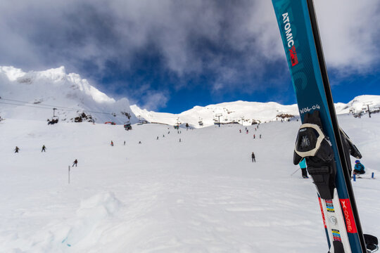 Skiers descend a snowy slope at Whakapapa Ski Area in New Zealand, with ski lifts running overhead and branded skis standing in the foreground