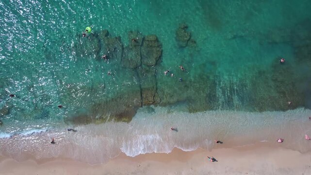 Beautiful aerial view of a sandy beach with crystal clear sea, turquoise water and visitors enjoying swimming and paddleboarding on Thassos Island, Greece.