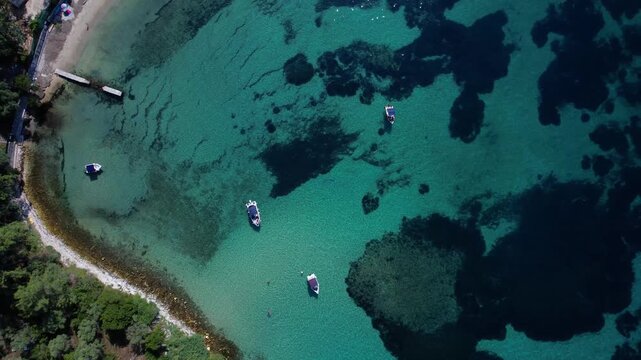 Aerial drone view of a crystal clear turquoise bay on Thassos Island, Greece, with swimmers, paddleboards and a sandy beach surrounded by rocky coastline on a sunny summer day.