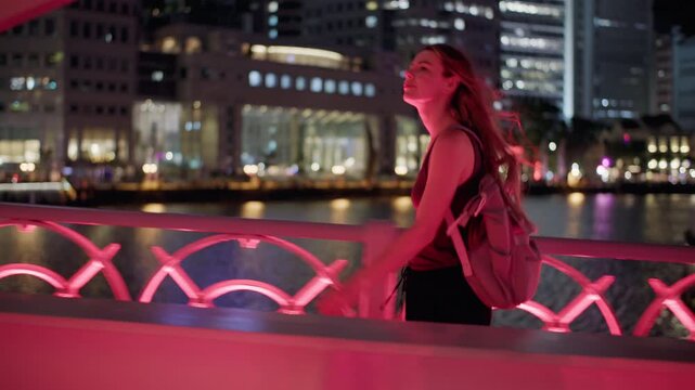 Happy female traveler crossing Cavenagh Bridge at night above the Singapore River with illuminated skyline and unforgettable metropolitan travel experience in Asia