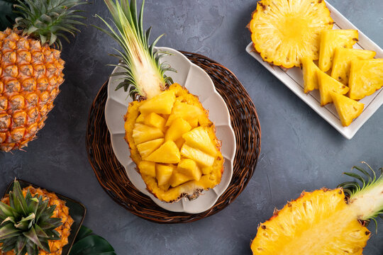 Fresh sliced pineapple fruits with green leaves on wooden board over dark gray textured background.