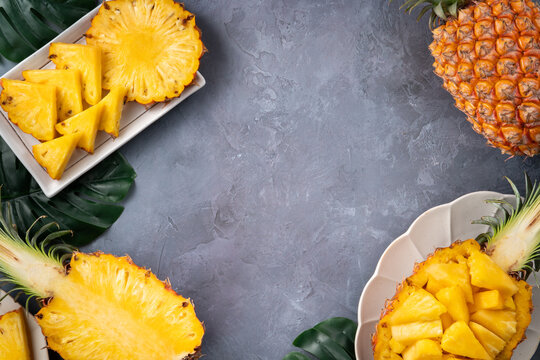 Fresh sliced pineapple fruits with green leaves on wooden board over dark gray textured background.