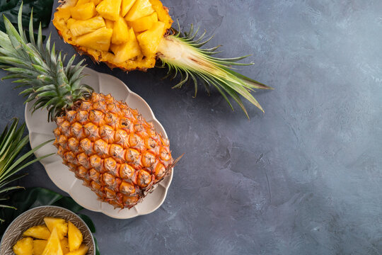 Fresh sliced pineapple fruits with green leaves on wooden board over dark gray textured background.