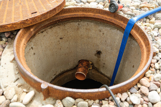 An open sewer manhole. A service cleaning of blocked sewer. A concrete septic tank with a plastic pipe. Rinse and pumping water out. Maintenance work, utility service, underground infrastructure.