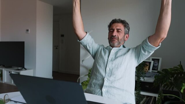 Tired man stretching his stiff neck and back at home office desk
