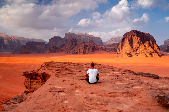 Man sitting on rock looks out at desert horizon with mountains, Wadi Rum, Jordan. Travel concept, nature, wildlife, Middle East.