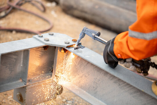 Worker cutting steel metal beam using oxy-acetylene torch on construction site