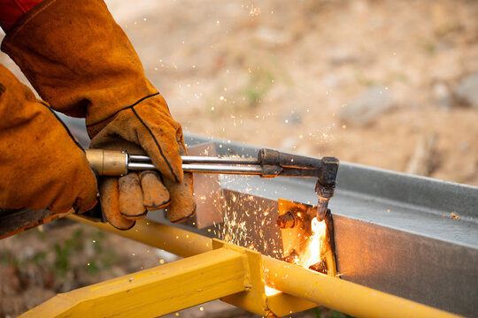 Bright sparks flying while worker cuts metal beam with torch on construction site