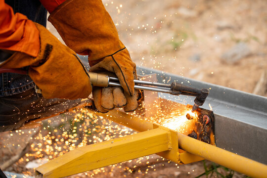 Worker using torch to cut off rusted nuts from metal frame structure