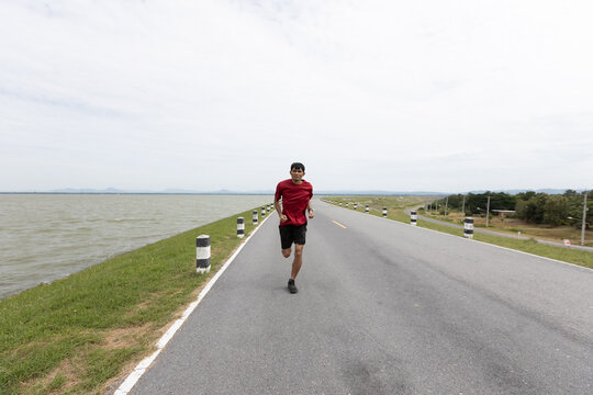 Asian male athlete running on an outdoor road, representing endurance, fitness, cardio exercise, active lifestyle, and running training.