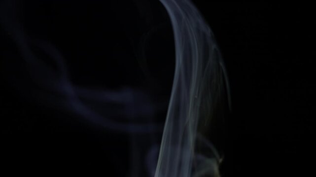 Wispy white smoke rises gracefully on a deep black background, creating an abstract and ethereal vapor texture. This atmospheric effect suggests air pollution, mystery, or a calming fragrance. The