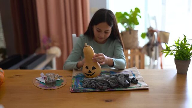 Female child painting pumpking during fall season for Halloween event - Holiday, childhood and autumn lifestyle concept	
