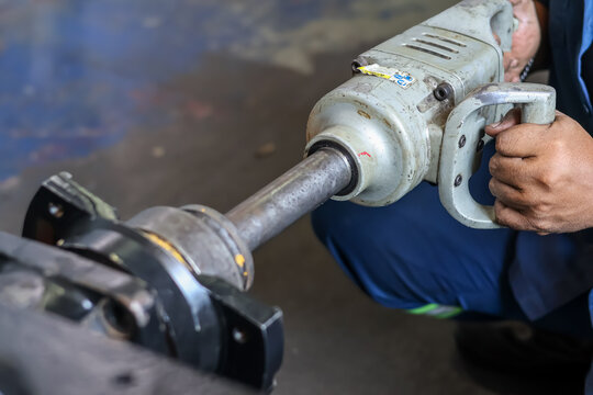 InduWorker using a pneumatic tapping machine and air tool for threading holes in metal mechanical components.strial pneumatic tapping machine in workshop.