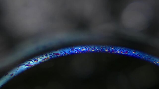 Iridescent soap bubble surface showing swirling rainbow colors and patterns in a macro close-up view against a dark background