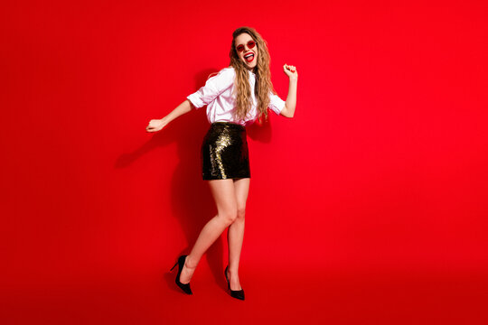 Joyful woman in stylish attire exudes charm and fun with dynamic pose on a vibrant red background