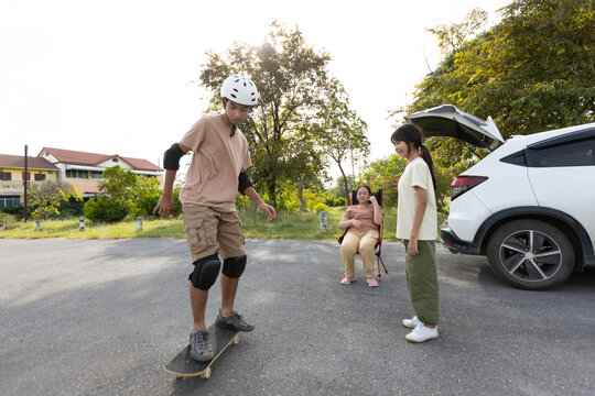 Teenage Asian Boy Skateboarding with Family Nearby Outdoors