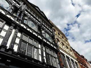 Obraz premium Historic black and white timber facade and Victorian brick buildings on a street in Manchester, UK under dramatic cloudy sky