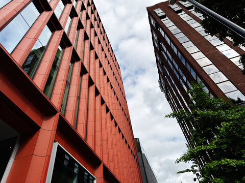 Modern red and brick office buildings with glass windows in Manchester, UK seen from a low angle with geometric facade and cloudy sky