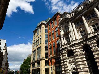 Obraz premium Street view of historic and modern office buildings in Manchester, UK with ornate stone facades and contemporary glass architecture under a bright blue sky