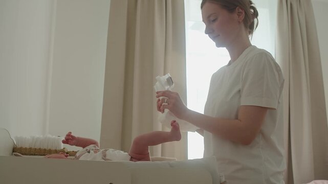 Mother opens clean diaper and arranges it before dressing baby on changing table. Preparation remains precise and unhurried, making hygiene routine smoother, safer, and more comfortable for infant.