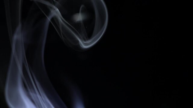Wispy white smoke rises and swirls on a dark black background, creating an abstract vapor texture. The ethereal atmosphere and fluid movement of the smoke provide a soft, smooth visual element. This