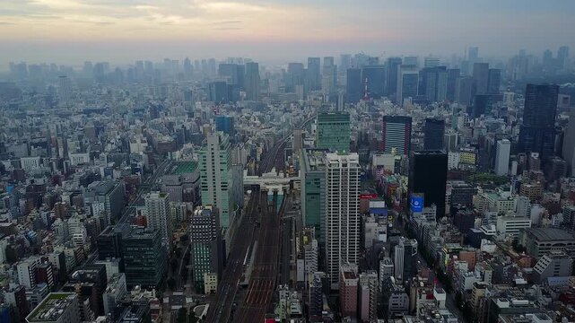 High-angle panoramic view of Tokyo, Japan, featuring railway tracks running through a dense urban cityscape surrounded by office buildings and skyscrapers during sunset. Modern metropolitan skyline fa