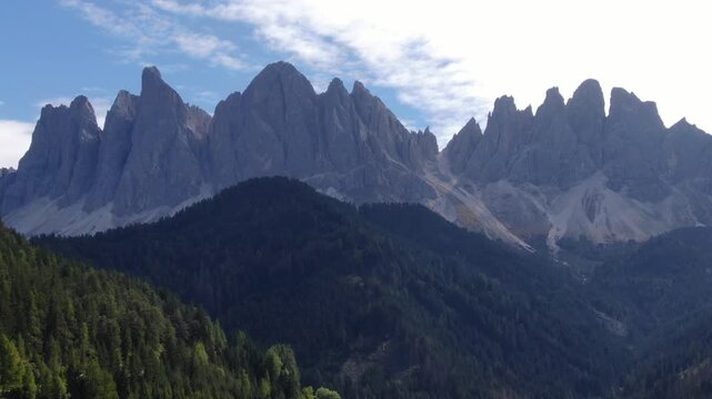 Cinematic Drone Shot Flying Over The Lush Green Pine Forests Of Santa Maddalena In Val Di Funes, With The Majestic Odle Mountain Peaks Rising In The Background. Drone Shot